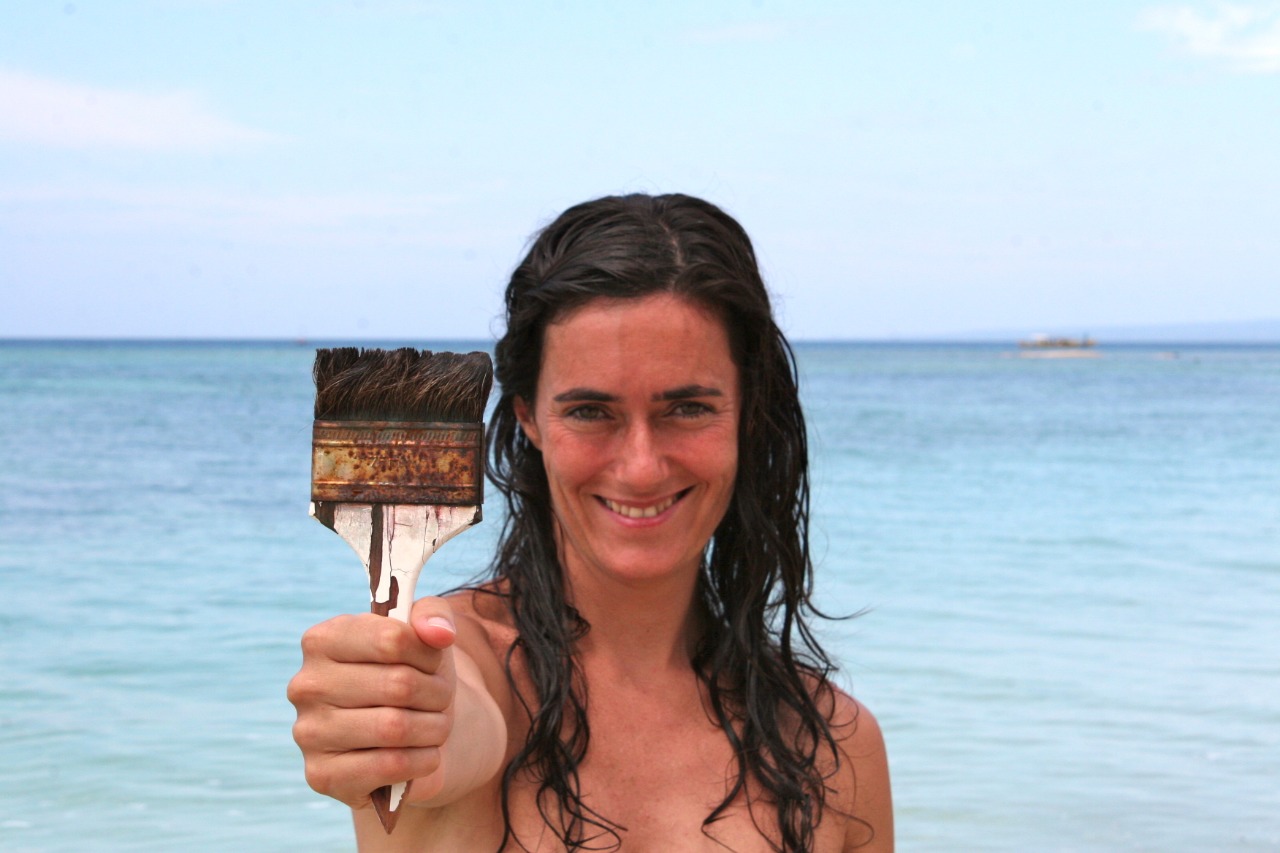 Brenda Rodríguez holding a large paintbrush by the water