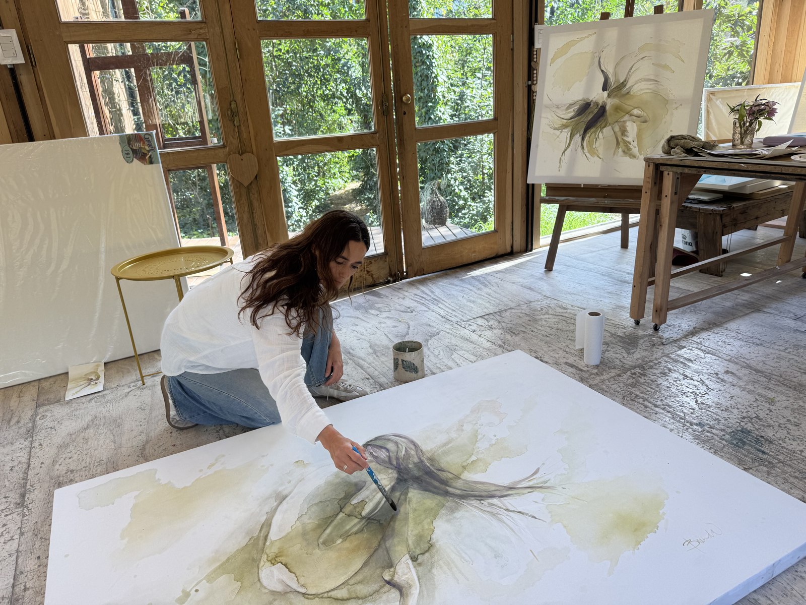 Brenda Rodríguez kneeling on her studio floor, painting with pigment and water